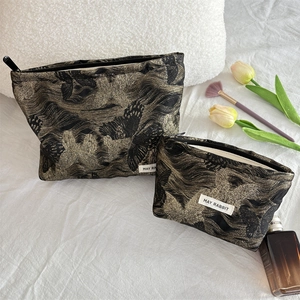 Detail of two black makeup bags with golden butterfly patterns on a white bed