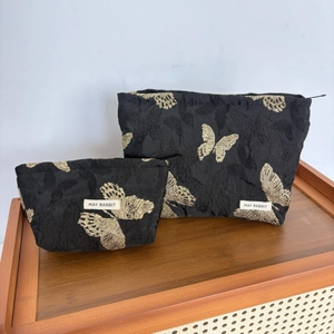 Detail of black trapezoid cosmetic bags with golden butterfly embroidery and zipper