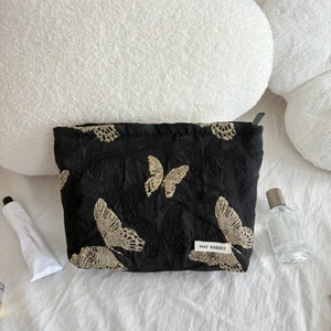 Detail of black makeup bag with gold butterfly embroidery and texture fabric