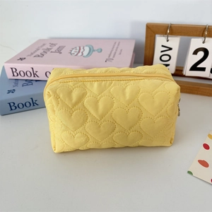 Detail of yellow quilted toiletry bag featuring heart embroidery and zipper closure