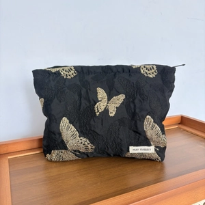 Detailed view of black makeup bag featuring golden butterfly embroidery and brand label