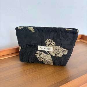Detail of premium black satin makeup bag featuring intricate golden butterfly embroidery