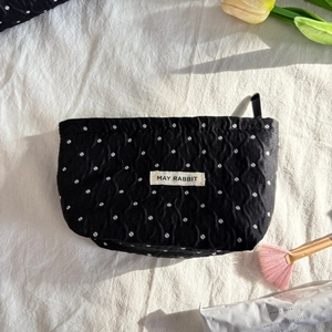 Polka dot makeup bag with textured fabric and logo label next to cosmetic items