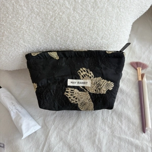 Detailed embroidery of gold butterflies on a black satin cosmetic bag with brand logo