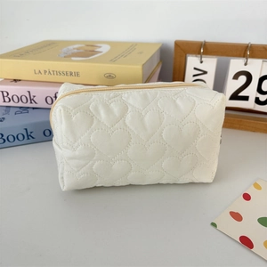 Detailed view of cream quilted makeup bag with heart patterns on a cozy vanity desk
