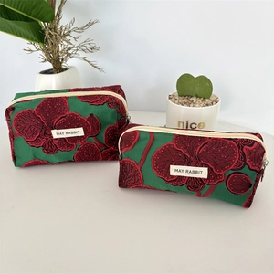 Détail de pochettes en jacquard vert avec broderie d'orchidées rouges et zips blancs