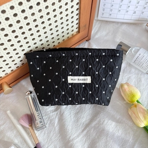 Detail of black polka dot makeup bag with wrinkled texture and brand woven label