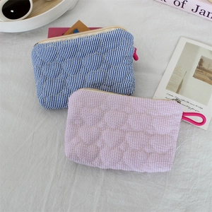 Close-up of heart-quilted striped pouches with long zipper pulls on a textured surface