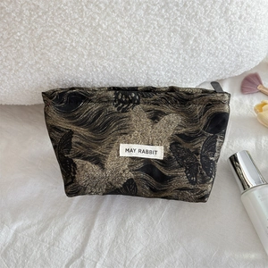Detail of cosmetic bag showing golden butterfly patterns and May Rabbit logo tag