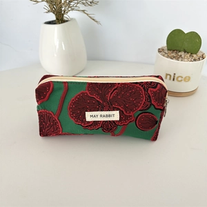 Détail de broderie d'orchidées rouge foncé sur une trousse en tissu vert avec fermeture