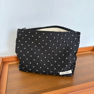 Close-up of black polka dot toiletry bag with zipper and woven brand label on wood tray