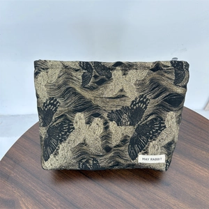 Detail of black and gold butterfly patterned makeup bag with brand label and sturdy zipper