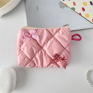 Detailed view of pink glossy quilted cosmetic pouch with cute bow accents on a desk