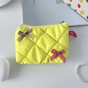 Flat lay of yellow quilted cosmetic bag with checkerboard bows on a white desk