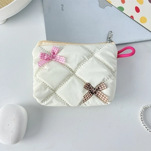 Detail of white quilted cosmetic bag with gingham bows on a lifestyle desktop