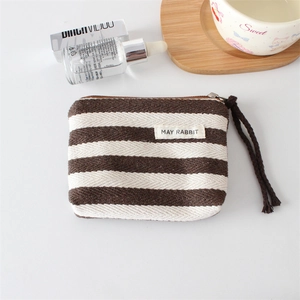 Detail of striped canvas coin purse with brand label, metal zipper, and brown wrist strap
