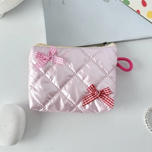 Detailed view of pink quilted lipstick bag with bow accents on a desk setup