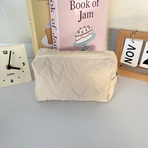 Close-up of beige wave-quilted toiletry bag with zipper closure on a cozy desktop