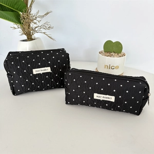 Détail de la trousse noire matelassée à pois avec étiquette blanche et fermeture éclair