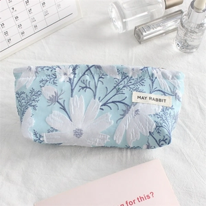 Flat lay of mini floral embroidered canvas makeup bag with small white daisy patterns