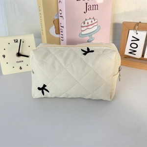 Detailed view of cream quilted makeup bag with bird embroidery and metal zipper pull