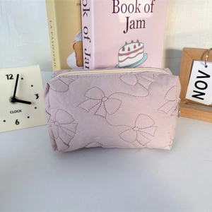 Detailed view of quilted lilac cosmetic bag with bow pattern embroidery and zipper