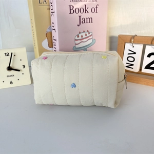 Macro view of beige quilted makeup bag with colorful heart embroidery and metal zipper