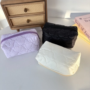 Detailed view of quilted heart pattern cosmetic bags in purple, black, and cream colors