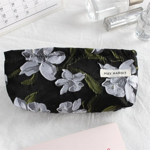 Detail of canvas makeup bag with floral embroidery, shown with lipstick and perfume