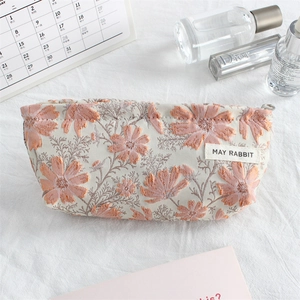 Detailed view of canvas makeup bag featuring pink daisy jacquard and brand tag