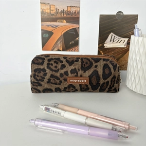 Detail of leopard print suede pencil case with leather logo and metal zipper on a desk