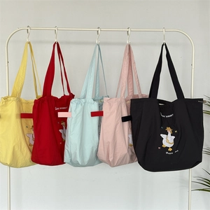 Detail of five colorful canvas tote bags with cute cartoon goose embroidery on a rack