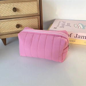 Pink quilted cosmetic bag with vertical stitching and metal zipper in a lifestyle setting
