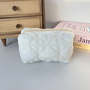 Close-up of white quilted makeup bag with silver ring zipper on vintage wooden desk