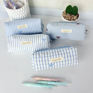 Detailed view of striped and plaid canvas pencil cases in soft pastel blue and white colors.