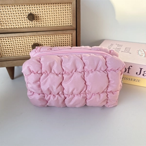 Detailed view of pink quilted cosmetic bag on a desk with soft light and aesthetic props