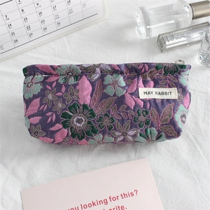 Detail of floral embroidery fabric and brand label on a purple jacquard canvas pouch
