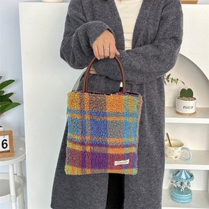 Detail view of colorful plaid plush tote bag with brown leather handles and brand label