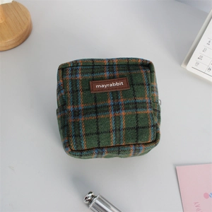 Détail de la trousse de maquillage en laine à carreaux verts avec étiquette logo