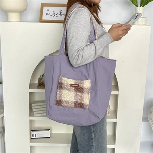 Detail of purple canvas tote bag featuring a brown plaid plush front pocket and leather tag