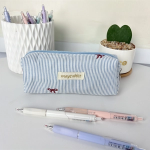 Close-up of blue striped pencil case with embroidered bow and brand label detail