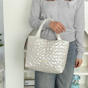 Detail of white quilted handbag with heart pattern stitching and woven brand label