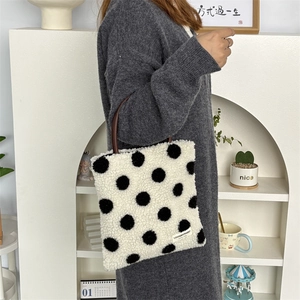 Detail of plush polka dot tote bag with brown handles and brand label on soft fabric