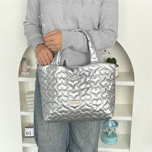Detail of silver quilted heart tote bag with metallic texture and gold logo plaque