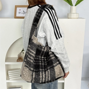 Close-up of plush plaid tote bag with wide shoulder strap worn by model in a soft setting