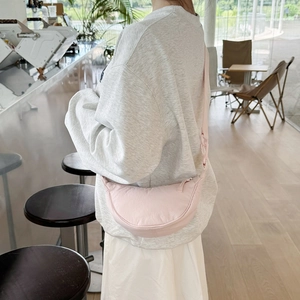Fashionable pink nylon crescent crossbody bag shown from a side view on a model