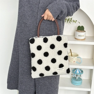 Detail of plush white polka dot tote bag with brown leather handles and woven label