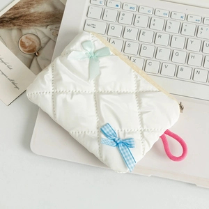 Detailed view of white quilted cosmetic bag with mint and plaid bow charms on a desk
