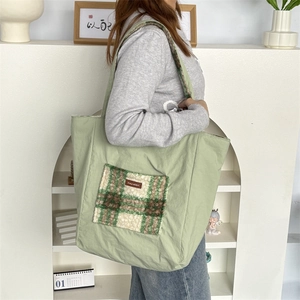 Close-up of a light green canvas tote bag featuring a checkered plush front pocket