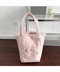 Pink plush tote bag with festive winter embroidery standing on a wooden floor